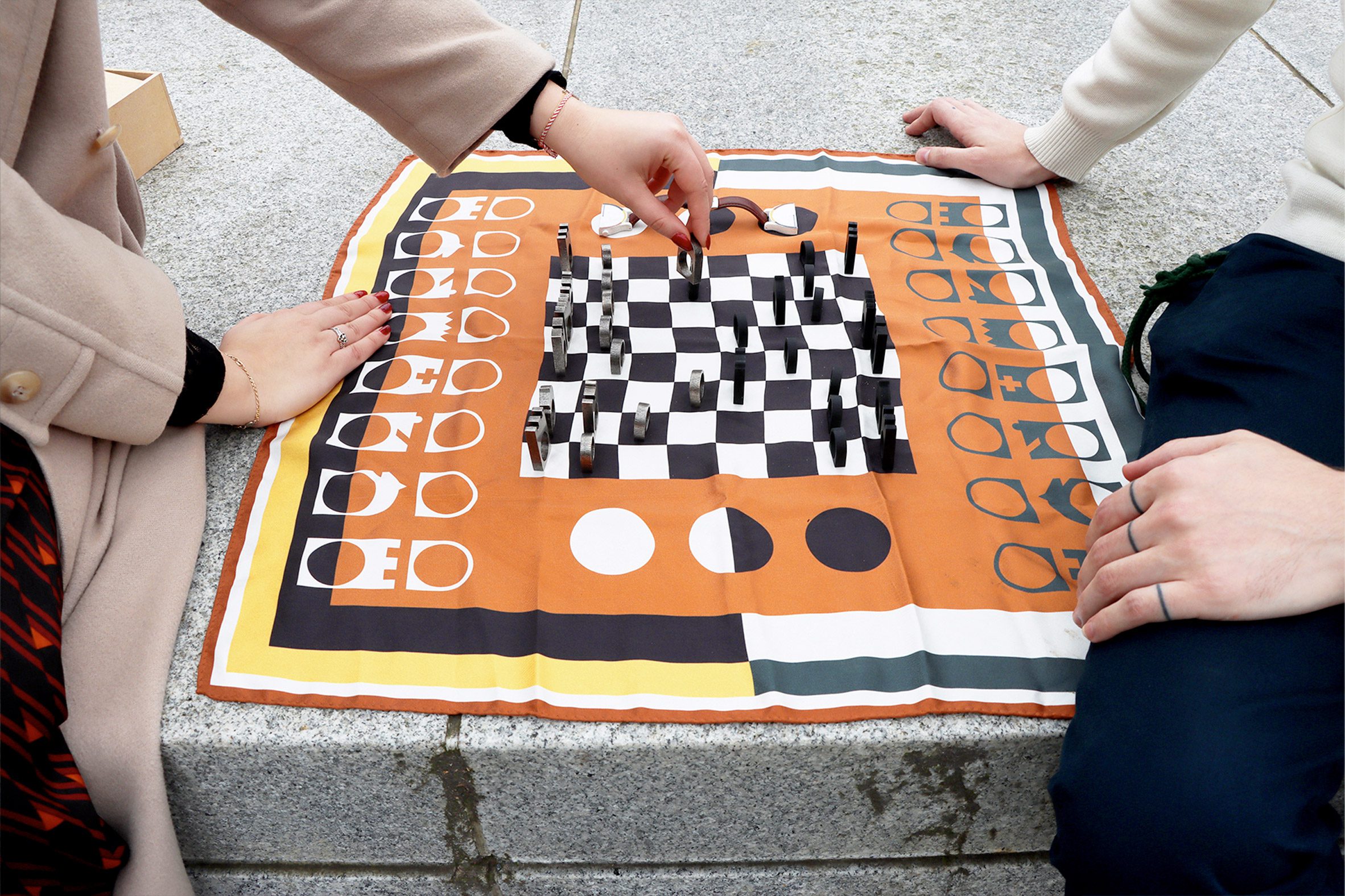 Photo of two people playing chess outdoors on a stylised silk board with sculptural pieces