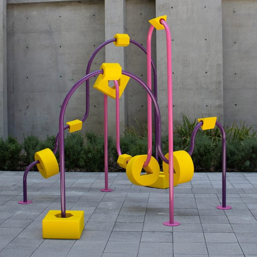 A photograph of an apparatus frame, in tones of pink and purple, within a grey concrete outdoor setting.