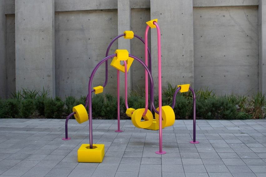 A photograph of an apparatus frame, in tones of pink and purple, within a grey concrete outdoor setting.