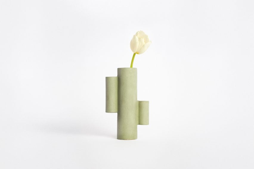 A photograph of a green ceramic vase which takes its shape from a cactus, with a white flower inside.