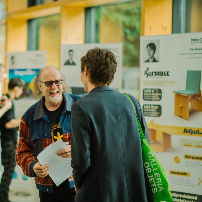 A photograph of two people interacting. There are large posters put up around them.