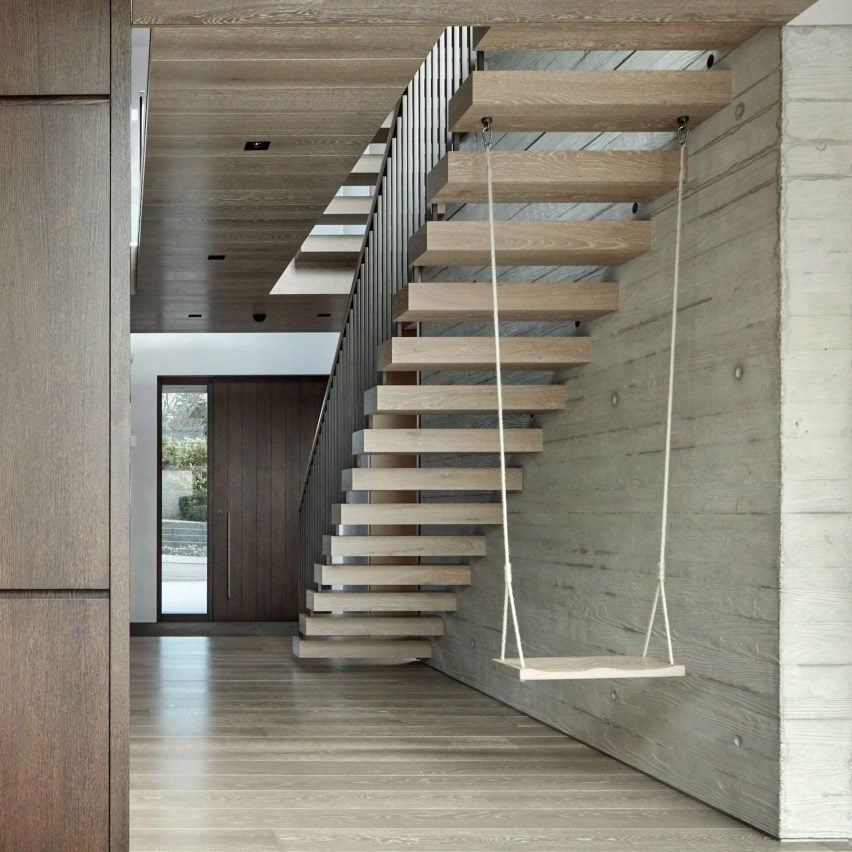 A photograph showing the underneath of a wooden floating staircase in tones of brown, with a white swing hanging from one of the stairs.