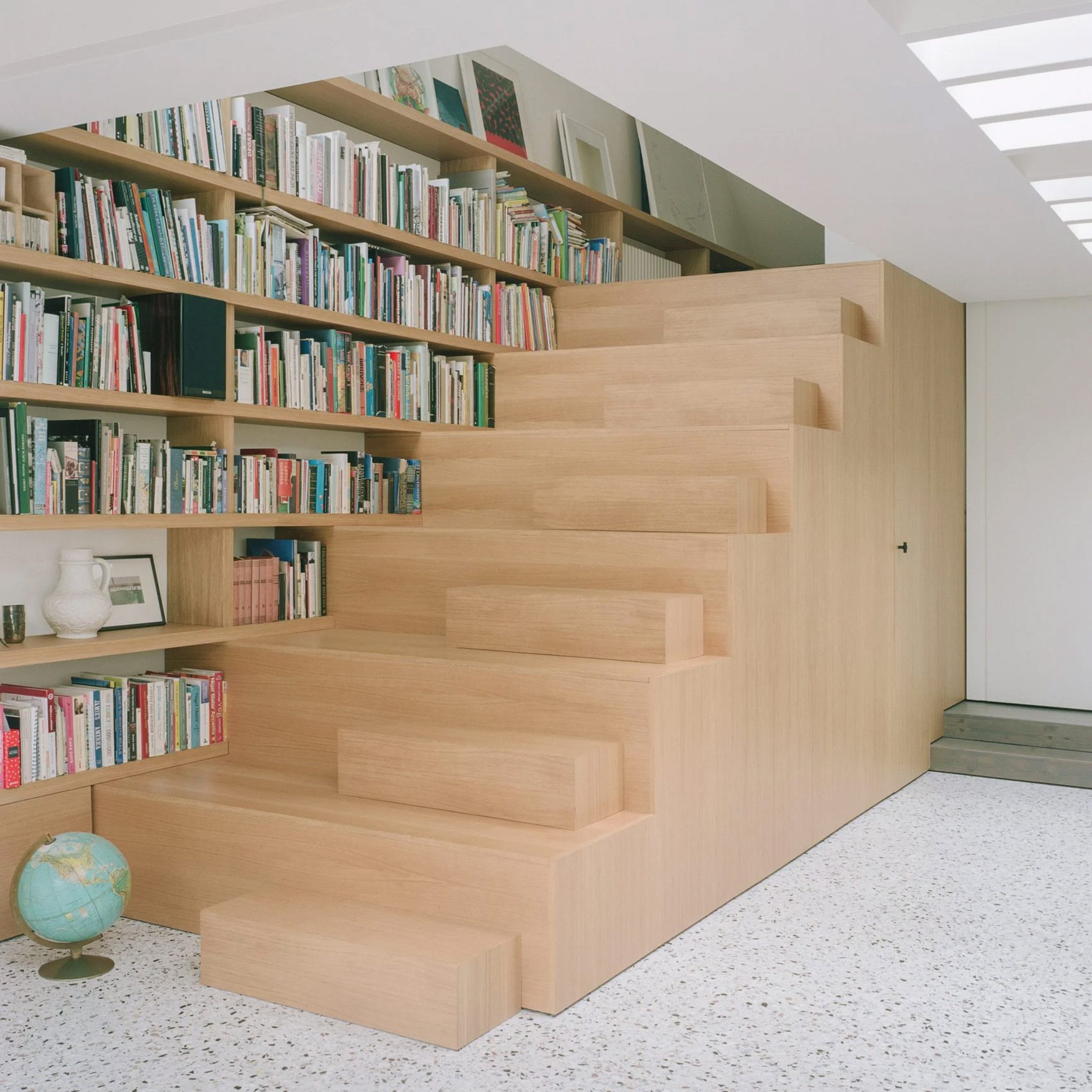 A photograph of a brown wooden staircase which sits against a bookshelf, with rectangular block on each of its steps that double as seats.