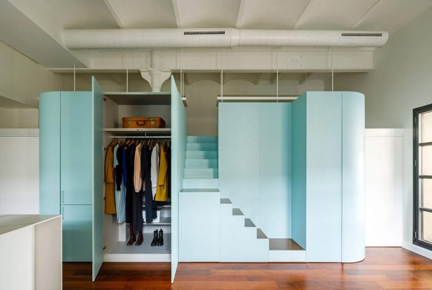 A photograph of a blue storage unit with a built in staircase and wardrobe, atop a brown wooden floor and with a white ceiling above it.