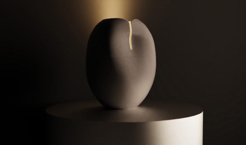 A photograph of a circular ceramic vessel in tones of grey, with an illuminated strip at its top. It is placed on a grey surface with a dark background behind it.