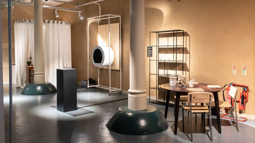 A photograph of a room in tones of grey and brown, with shelving, tables and chairs in the space.