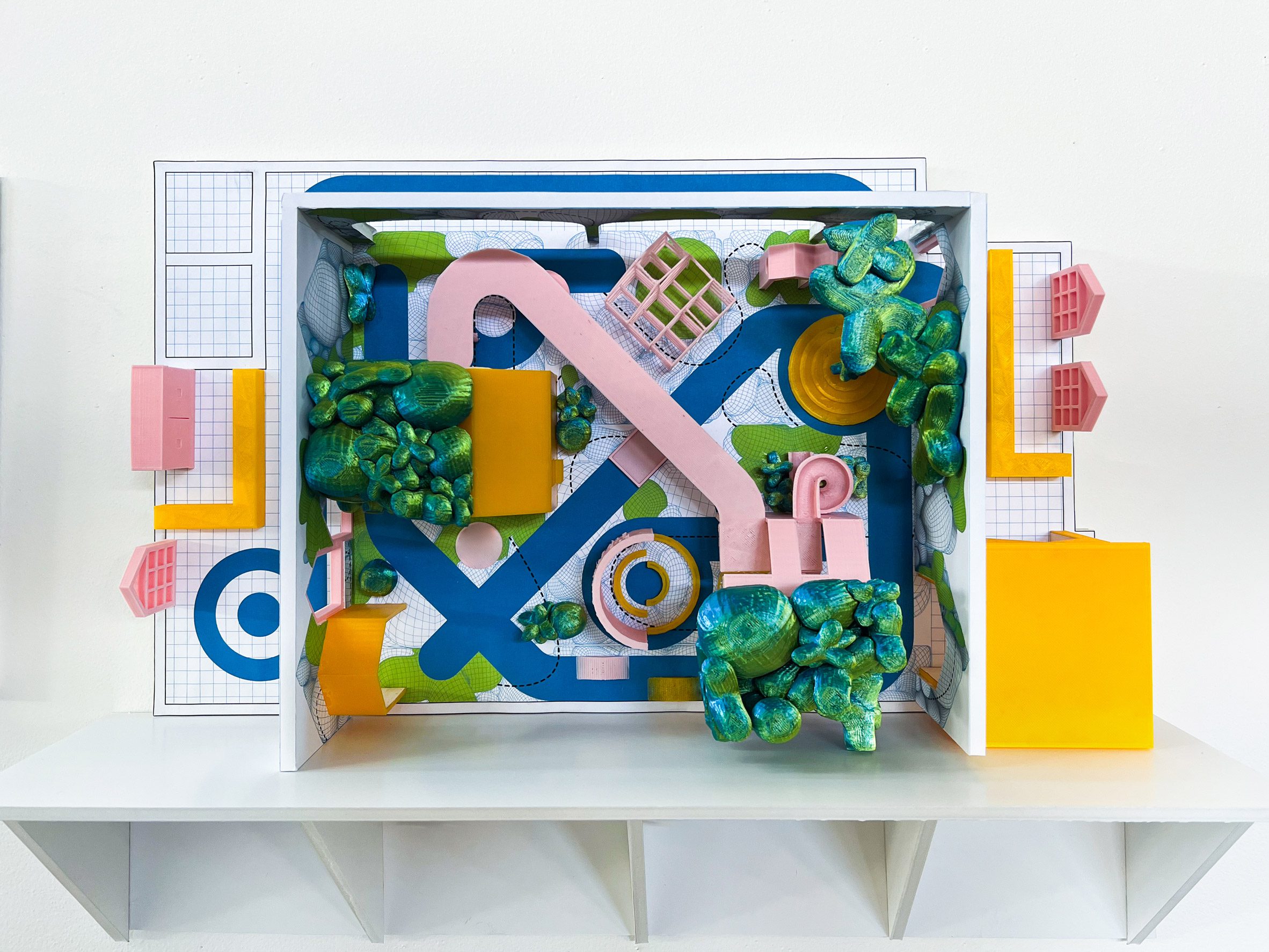 A photograph of an architectural model from above of a playground design, which features tones of pink, blue, green and yellow.