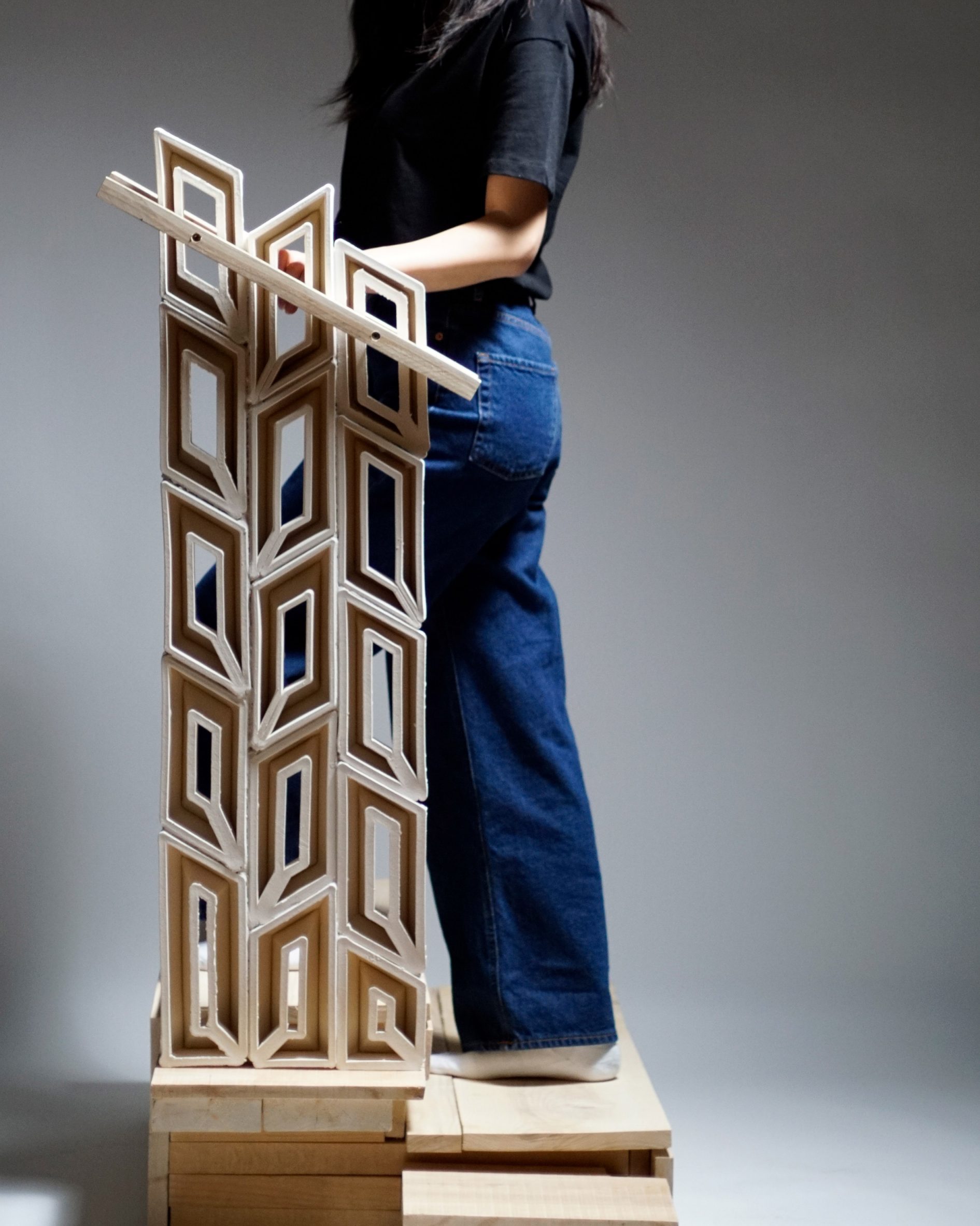 A photograph of a person standing next to a brown wooden sculpture which consists of multiple irregular rectangular shapes. 