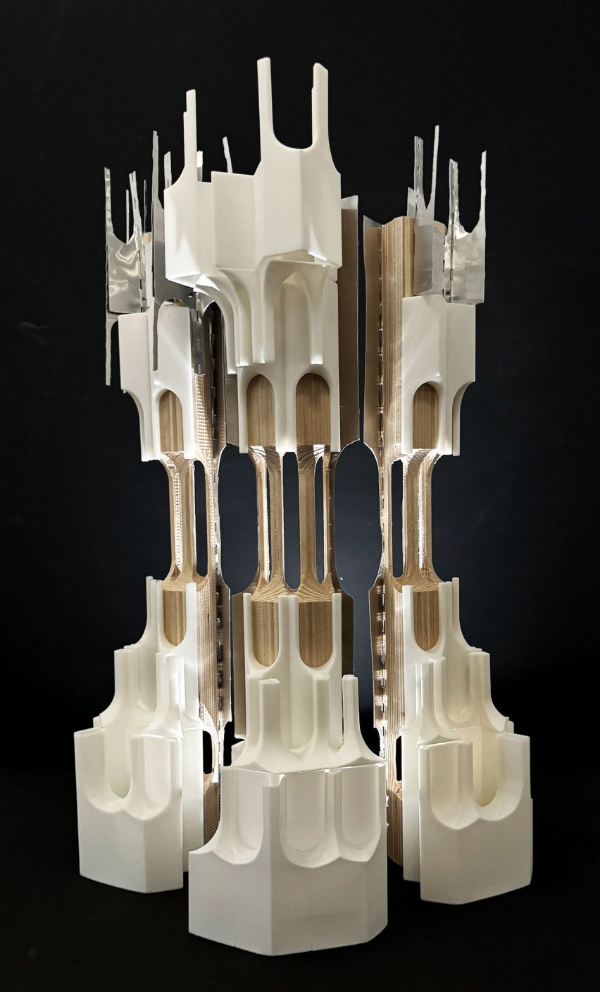 A photograph of an architectural model in tones of white and beige, in a complex geometric form, against a black backdrop.