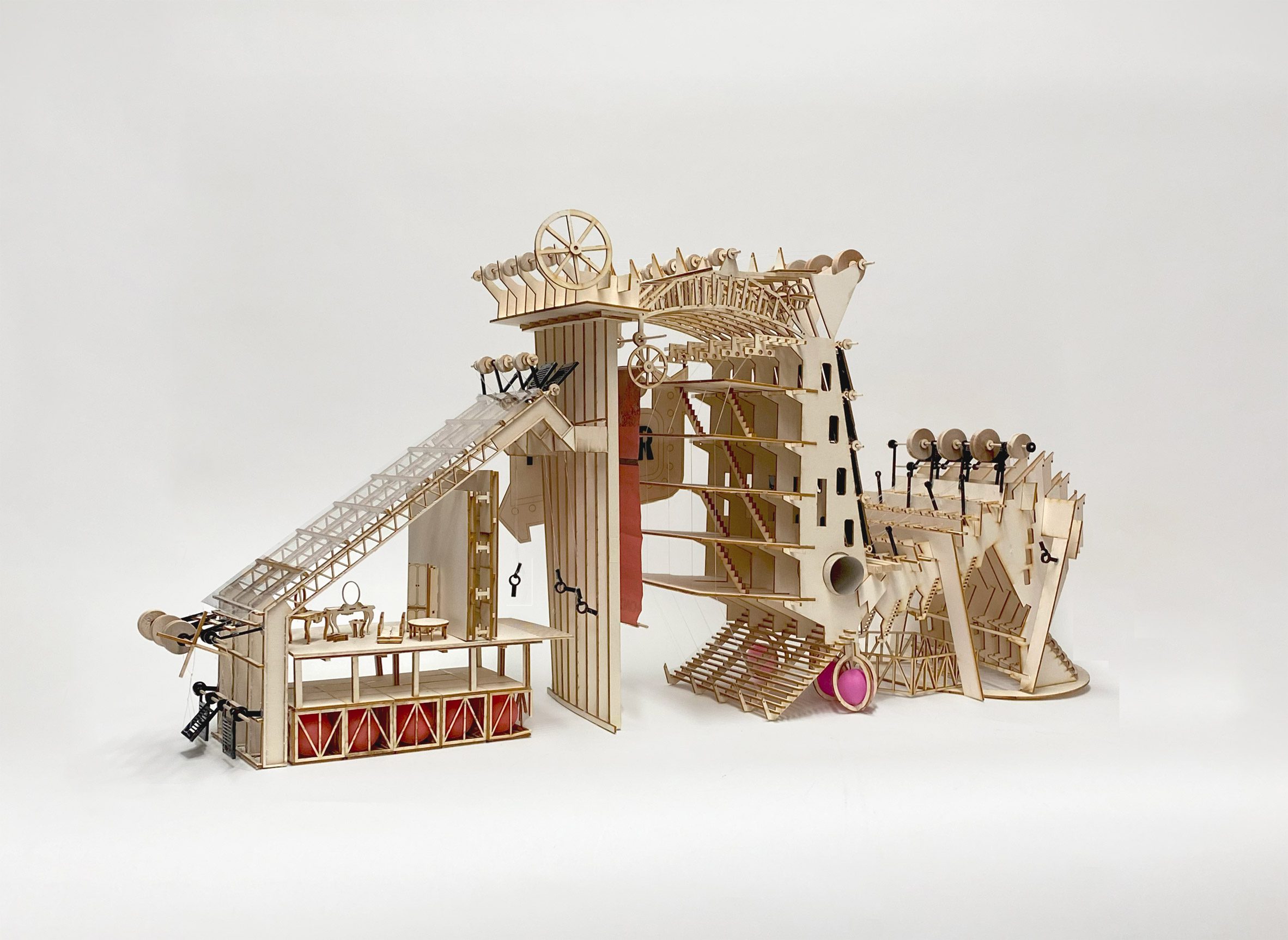 A photograph of a wooden architectural model in tones of beige, red and pink, against a white backdrop.