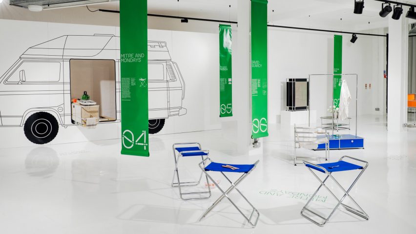 A photograph of a furniture exhibition, with a white floor and walls and green rectangular banners hanging from the ceiling.