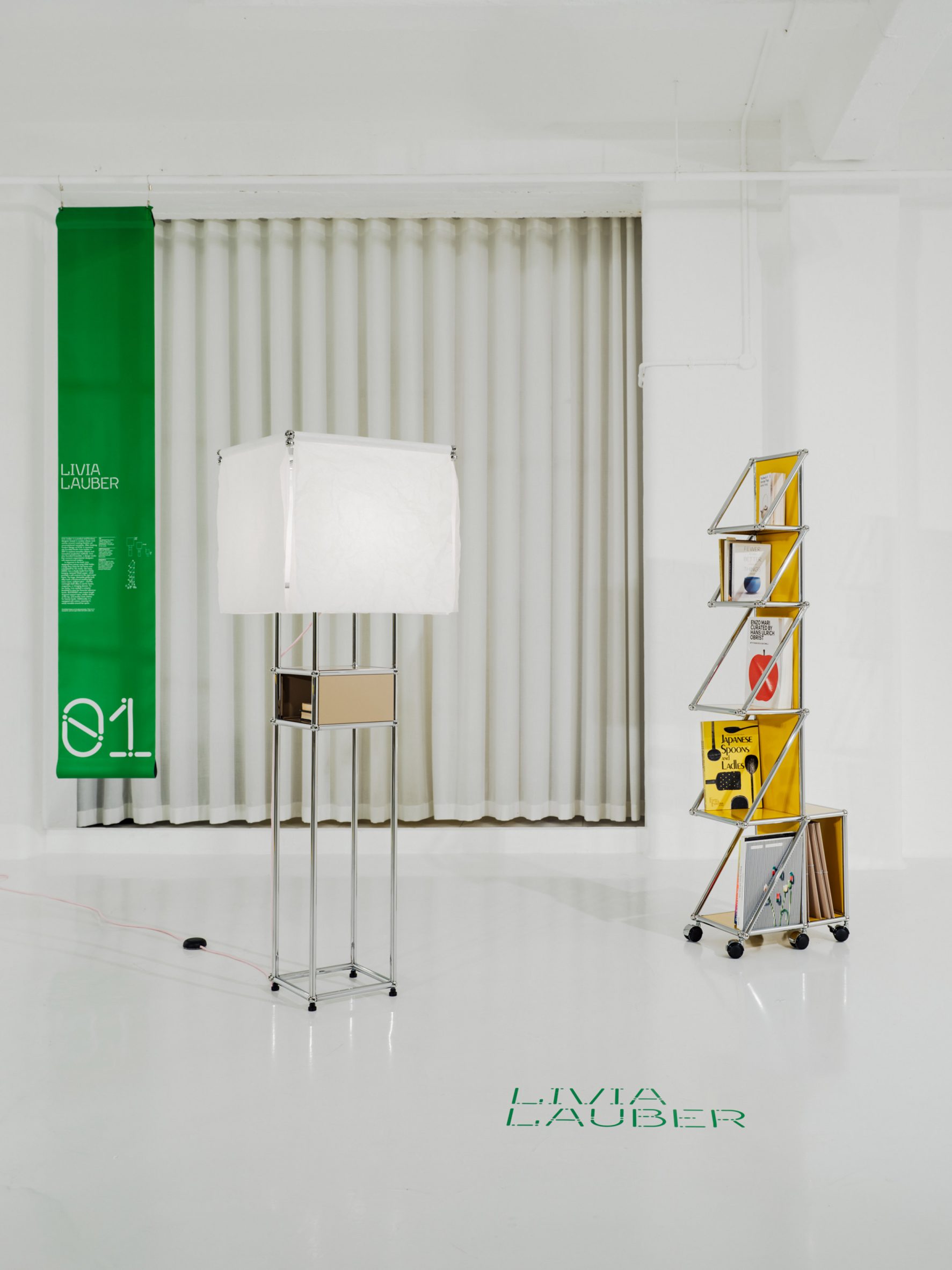 A photograph of a rectangular lamp, with a white lampshade and structured with silver beams. There is a yellow bookshelf to the right of it, also structured with silver beams.