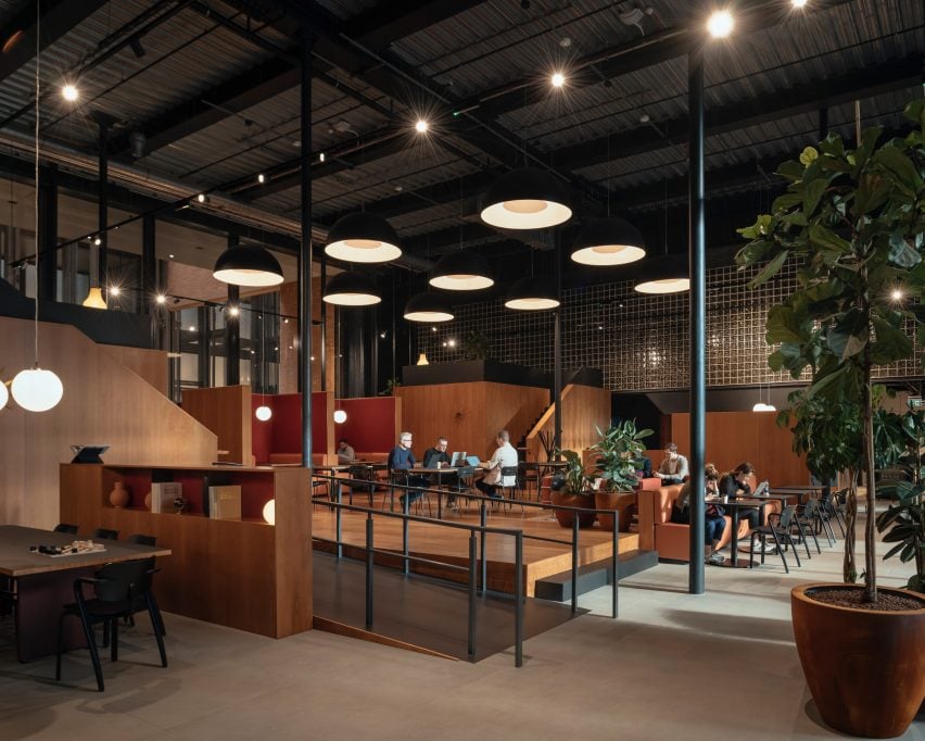 A photograph of a workplace/cafe in tones of brown and red, with people sat at tables.