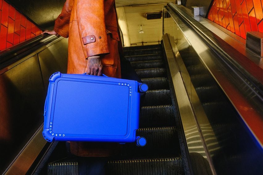 Photo of a person from the torso down carrying a bright blue Casetify suitcase on an escalator