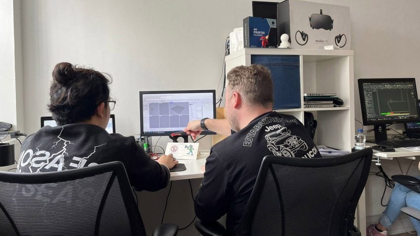 A photograph from behind of two people sat at a desk with a computer.