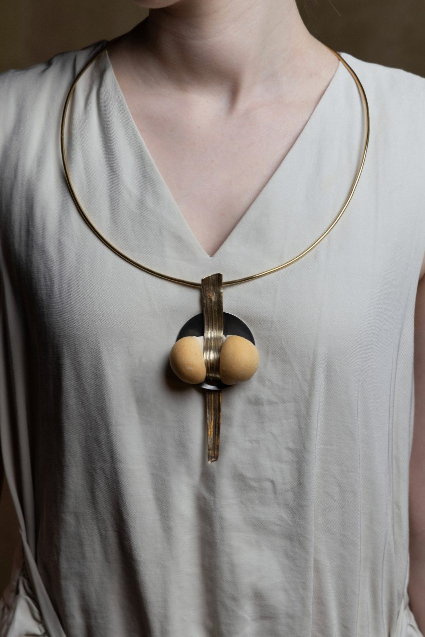 Photo of a woman's torso with a chunky pendant formed from a ball of baked dough pressed through the centre by a long, textured metal element by Cindy Xinyi Wu