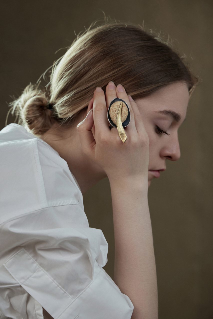 Photo of a woman wearing a large sculptural ring made from two metal elements with a ball of baked bread dough compressed between them