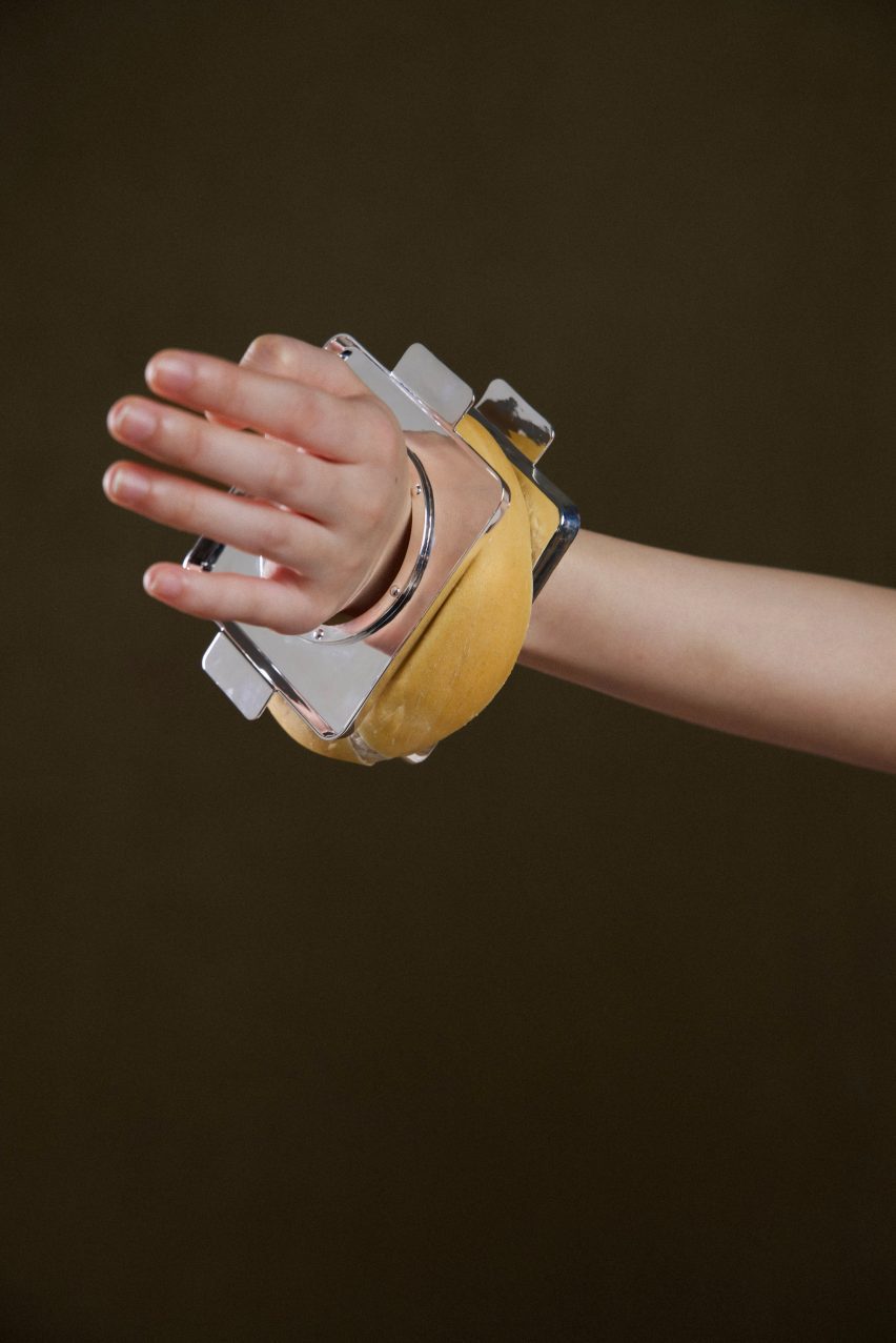 Photo of a person's wrist wearing a chunky bangle made of two pieces of square, flat, shiny silver metal with a bagel-like baked dough form pressed in between