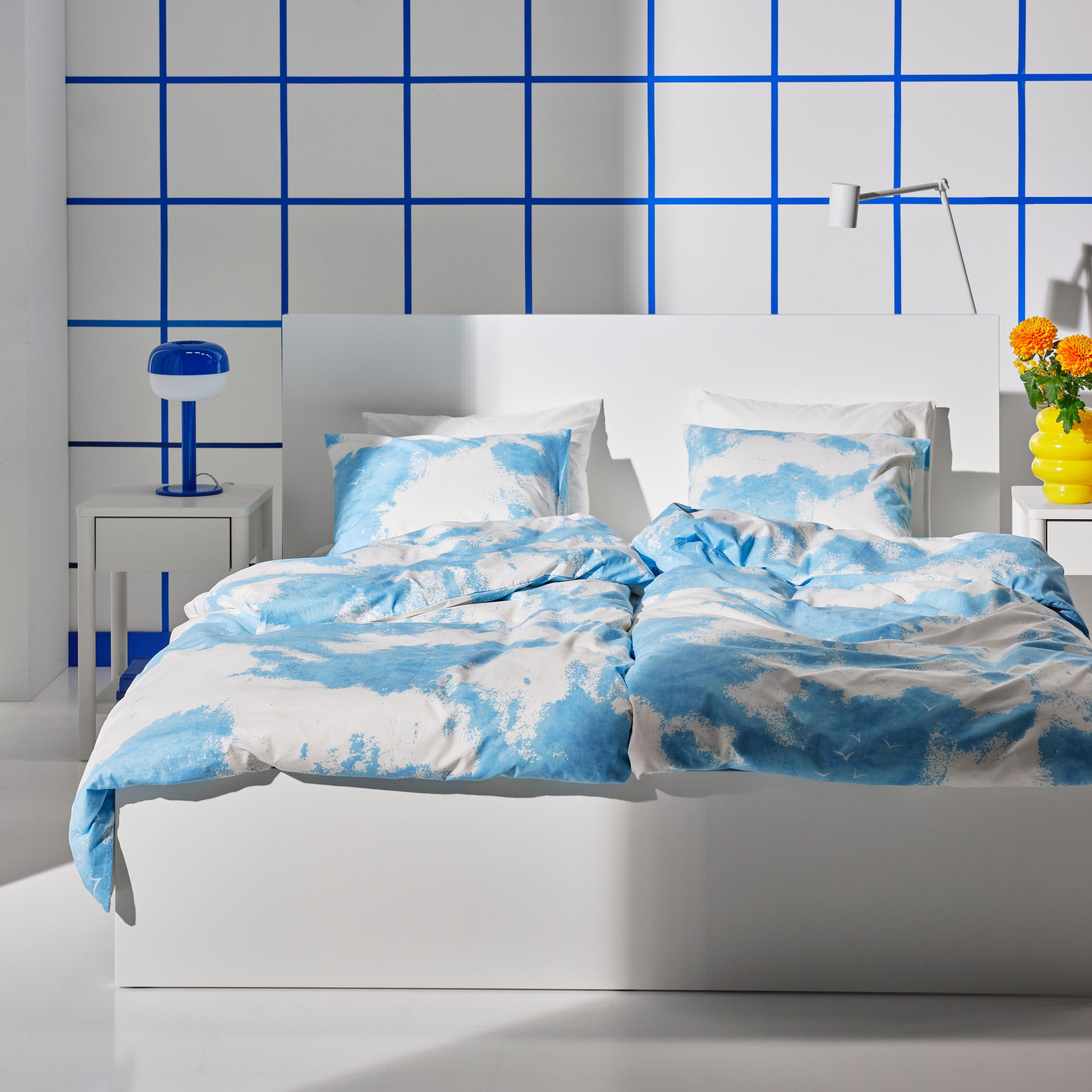 Photo of a white bed covered with the IKEA Ängsvitvinge bed linen with a blue-and-white cloud print