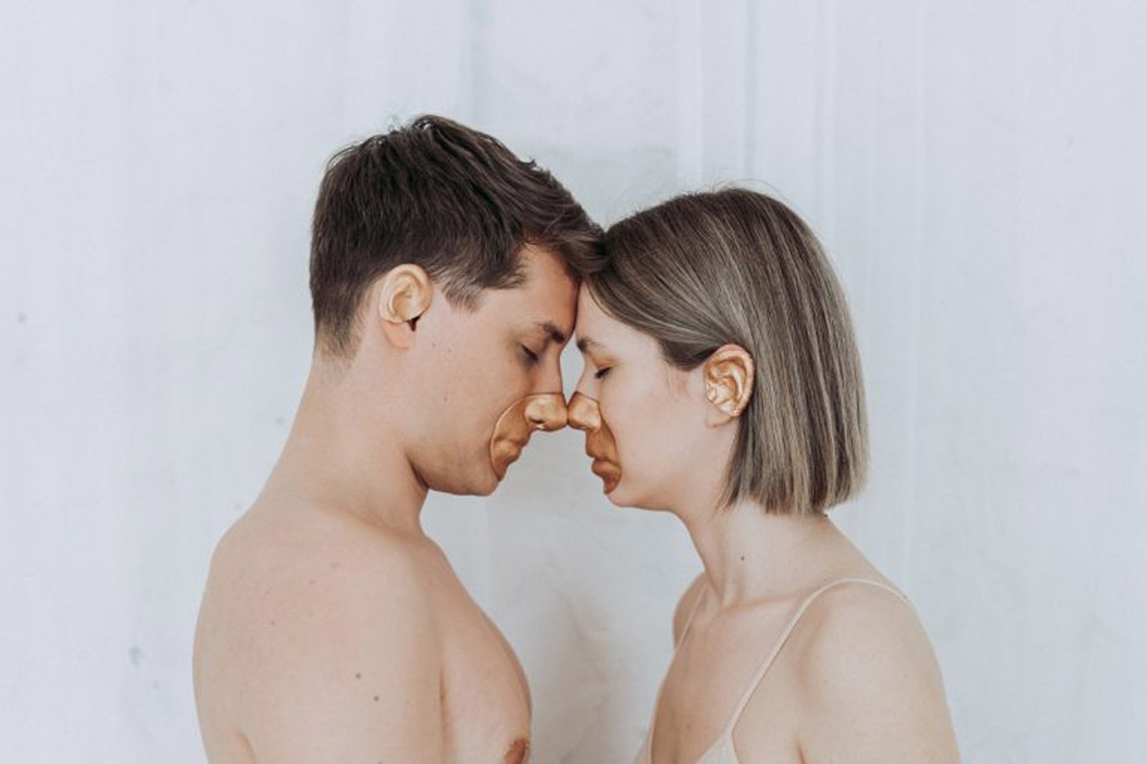 A photograph of two people facing one another, with copper-coloured paint over their noses and lips.