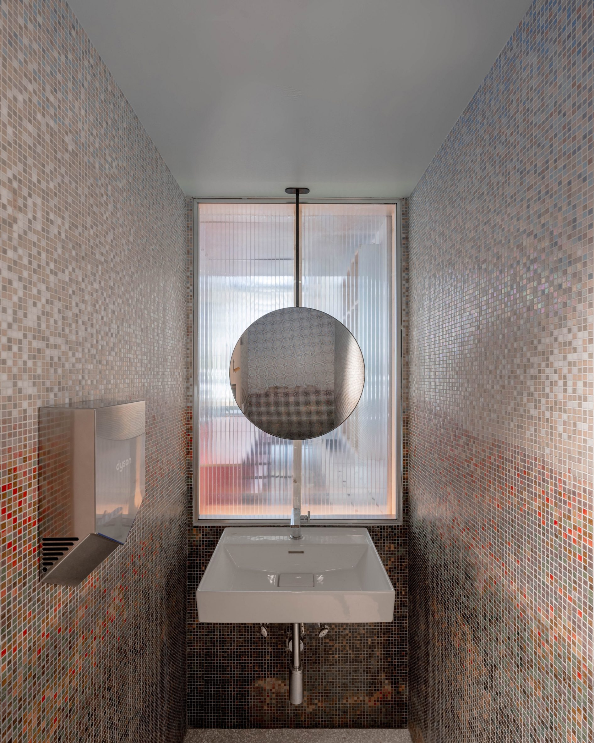 Bathroom lined with mosaic tiles, with a circular mirror over the basin