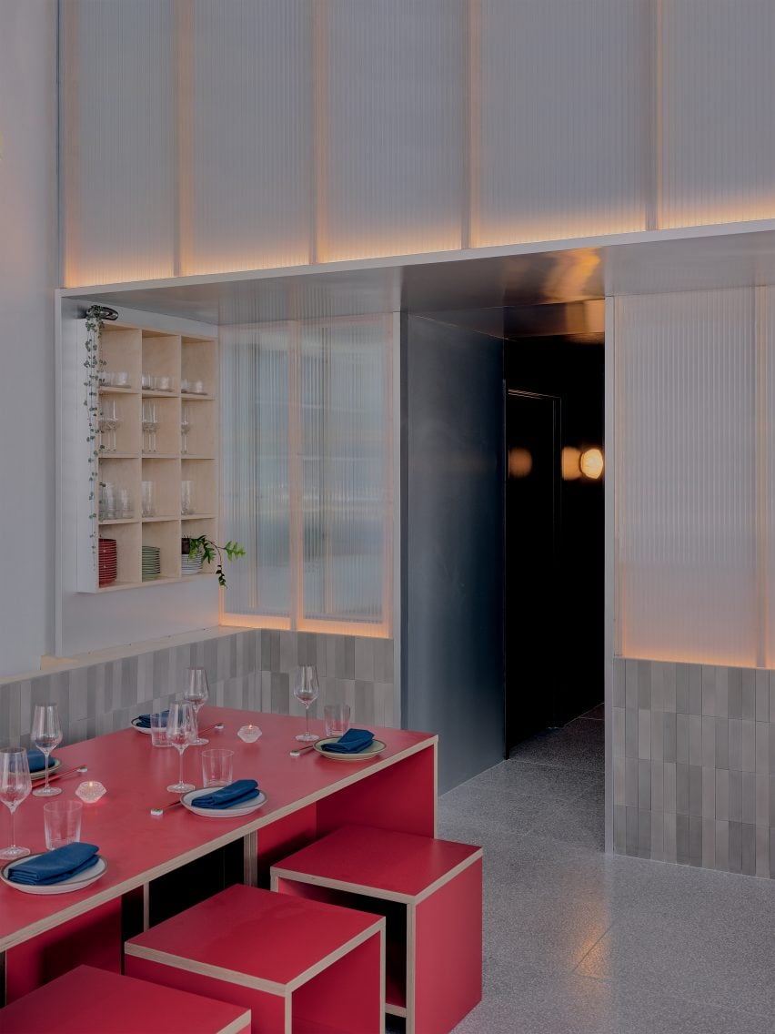 A long red tables with matching stools in front of glowing polycarbonate panels