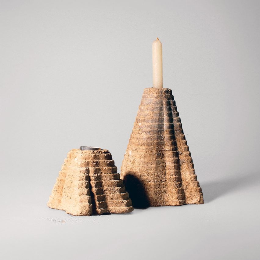 A photograph of two candle holders in pyramid-like structures, in tones of beige. One has a white candlestick in it.