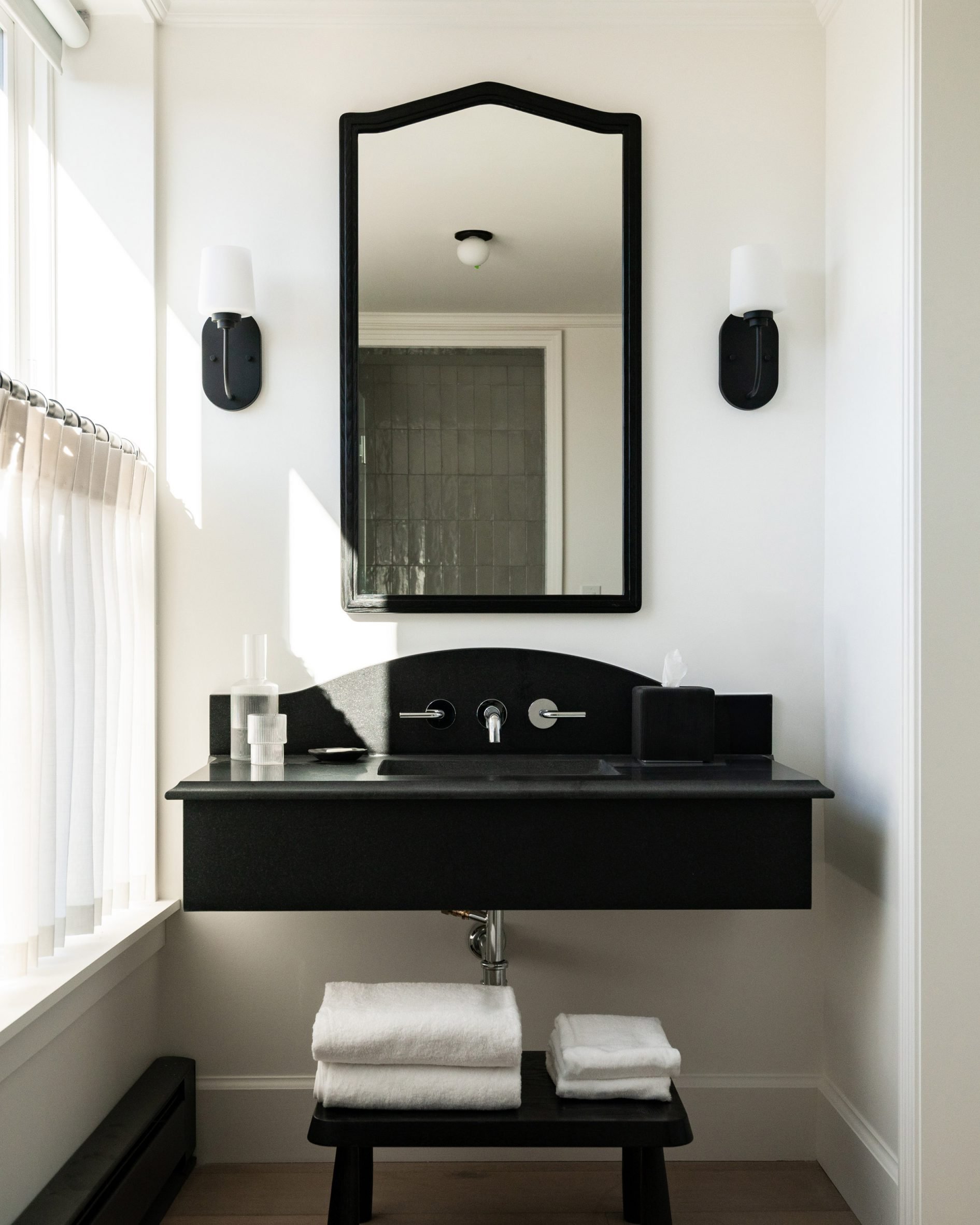 White bathroom with a black sink, mirror frame and sconces