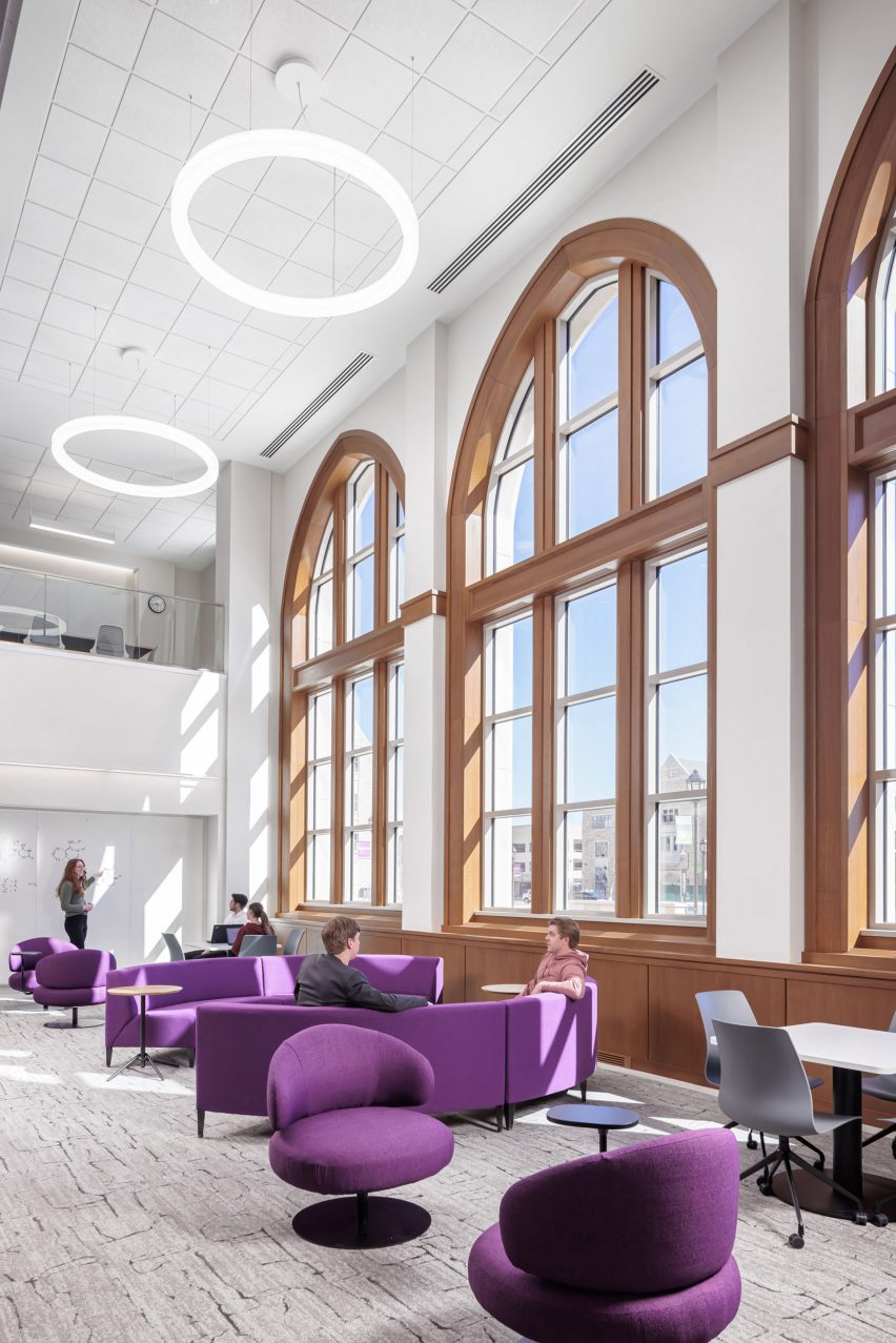 Double-height lounge space with purple furniture and pointed-arch windows