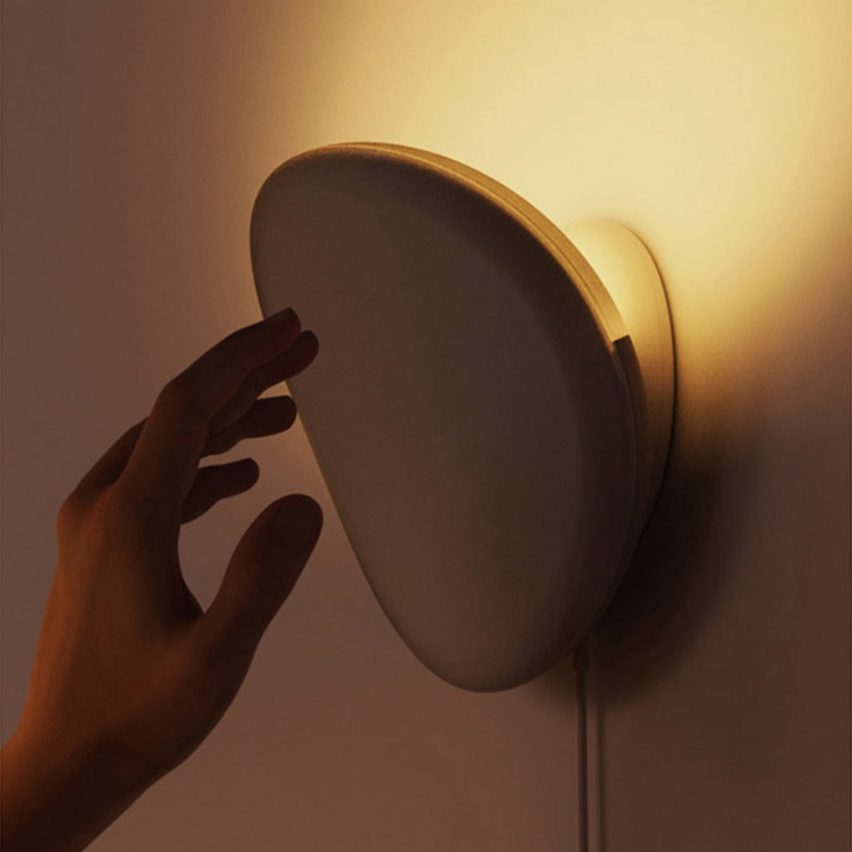 A photograph of a person's hand interacting with a circular light on a wall.