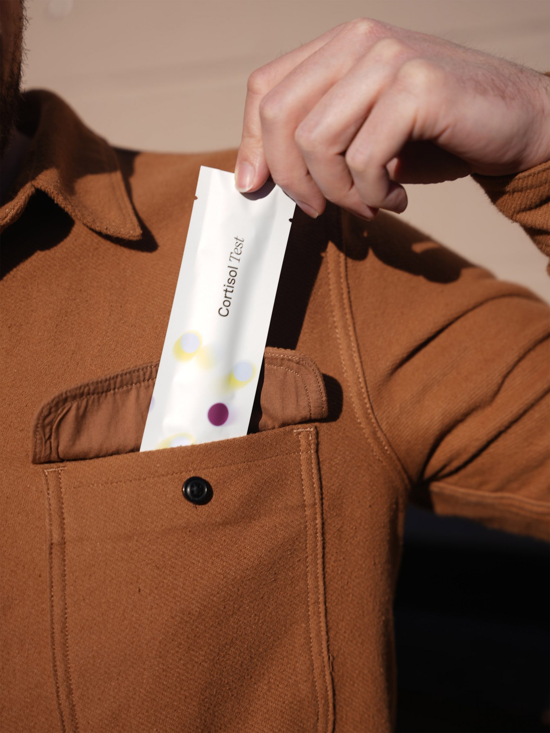 Close-up photo of a person sliding a packaged item reading 'cortisol test' into the front pocket of their shirt