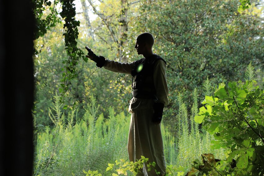 Man holding up his hand to touch a plant while wearing the Gaia vest