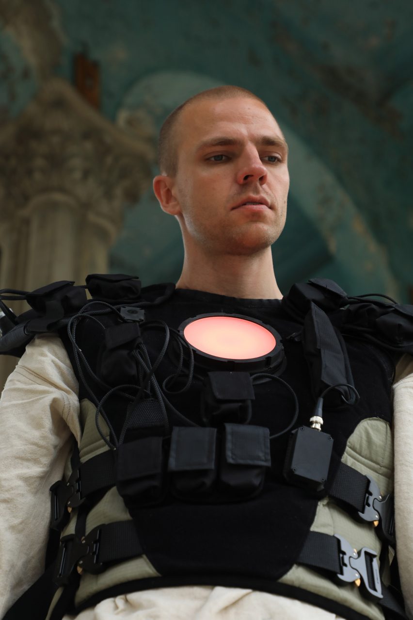 Photo of a man wearing a black vest similar to a flak jacket but with a circular LED light over the heart and several wires attaching to various small pockets