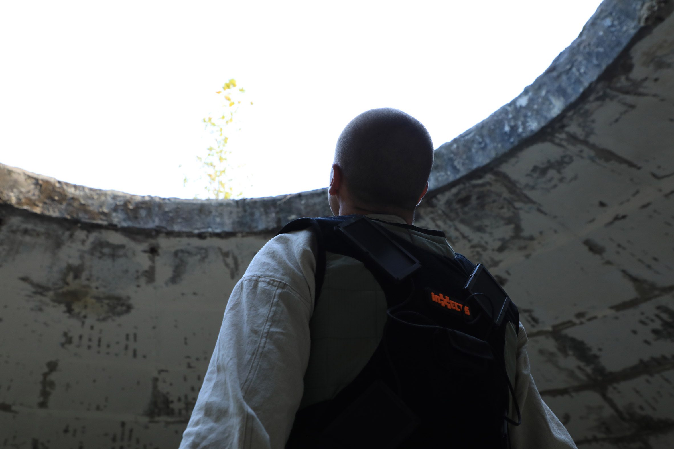 Photo of a man shot from behind as he looks up through a big round skylight in a dilapidated building