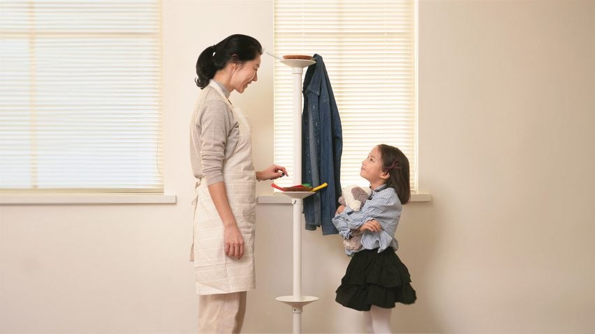 A photograph of a child looking up at an adult, stood in front of a white wall.