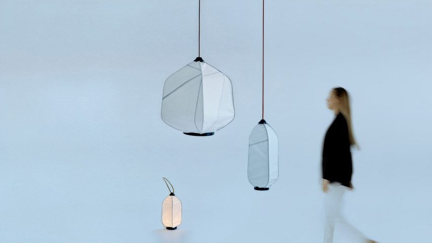 A photograph of three lamps crafted from sailcloth, two are suspended via black cords and another on the floor, illuminated. There is a person walking towards them.