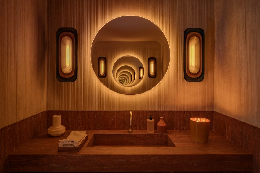 Bathroom with ribbed wall coverings and a frameless circular mirrors above a dark pink stone sink