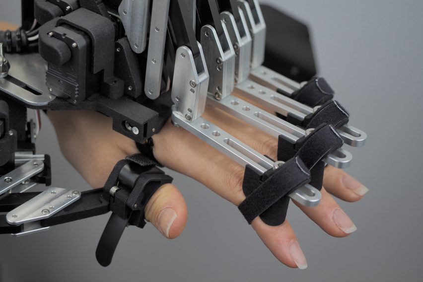 Close-up photo of a hand wearing a complex exoskeleton with motors attached to each of their fingers