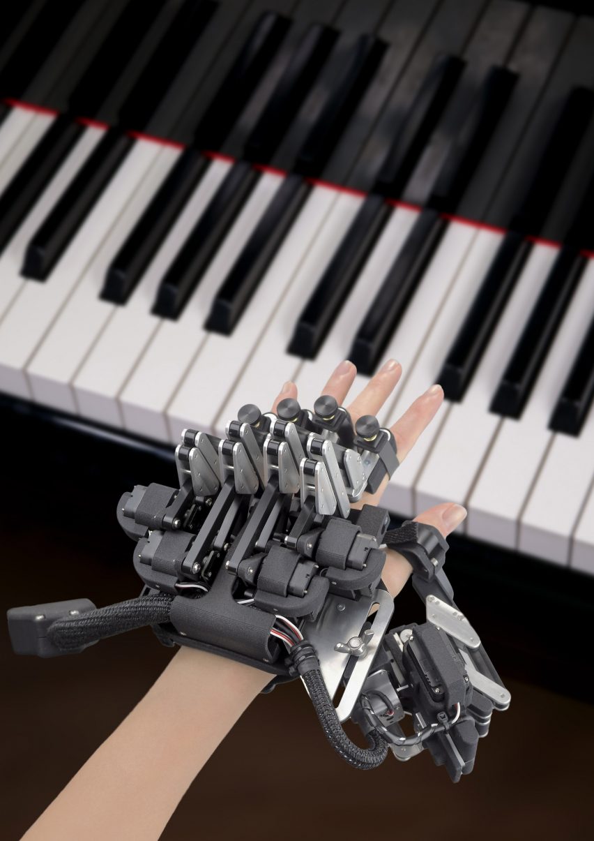 Photo of a hand hovering over piano keys while wearing a complex exoskeleton
