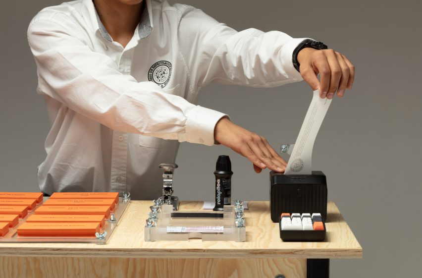 A photograph of a person wearing a white shirt, interacting with a design installation, which is situated atop a desk.
