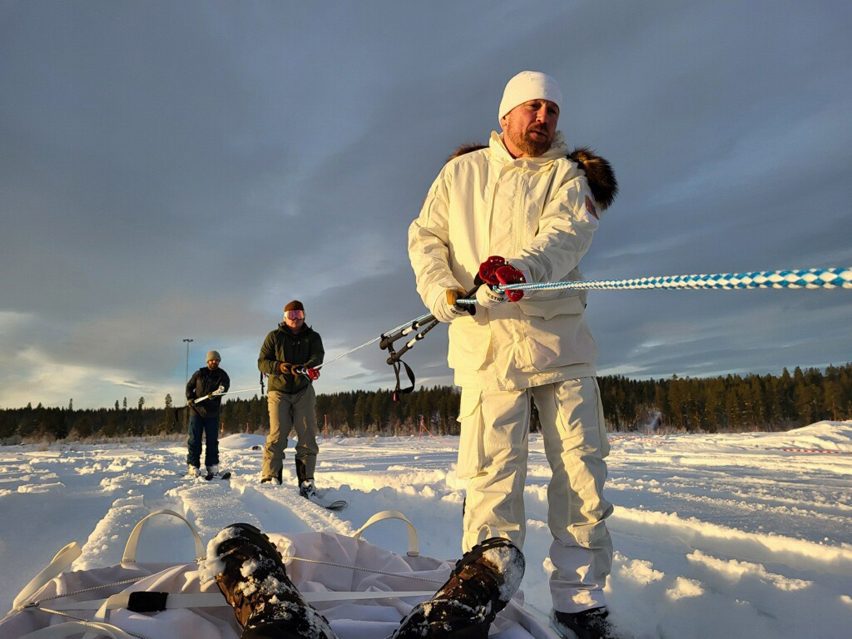 Photo of men in snow suits pulling on a length of rope in a snowy field