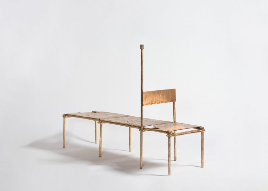 Studio photo of a daybed made from cast copper. At one end a backrest forms a chair, while a linear element extending vertically from the frame adds a candlestick