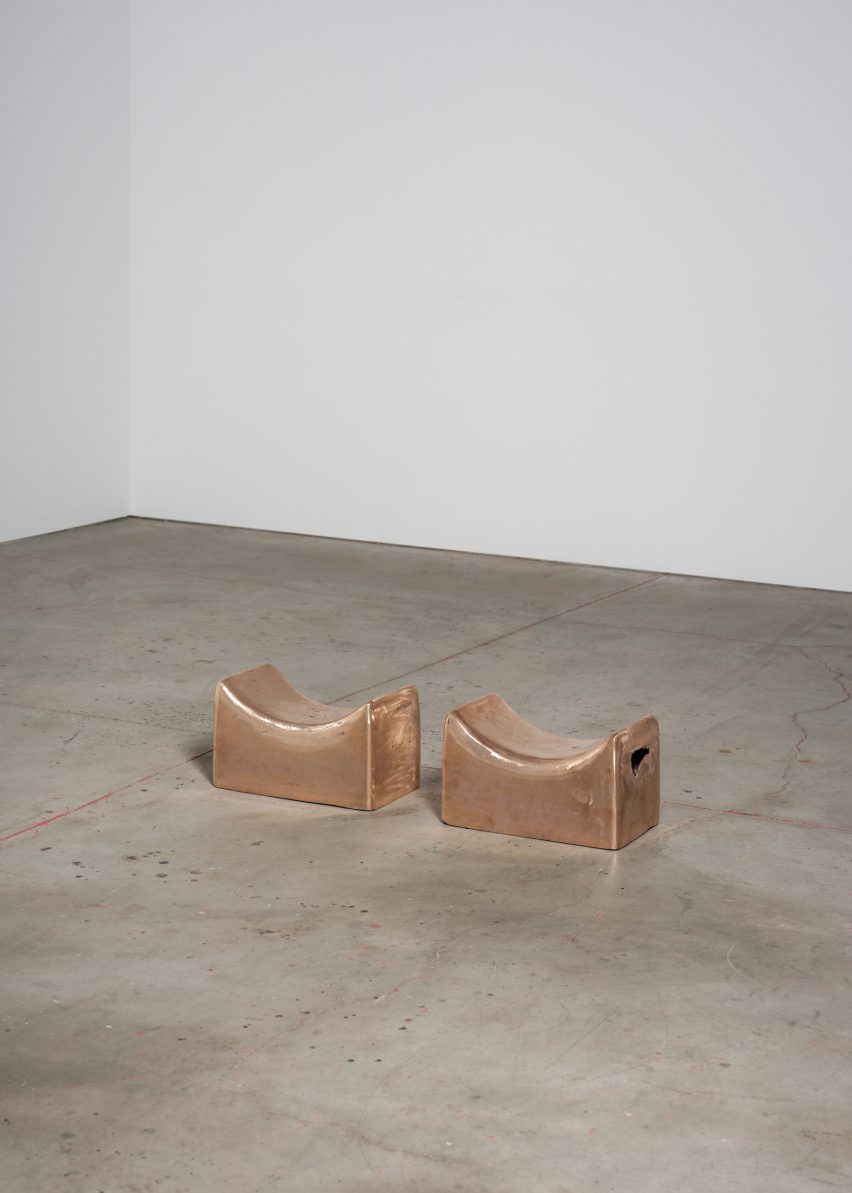 Photo of two copper headrests sitting lined up on a concrete gallery floor
