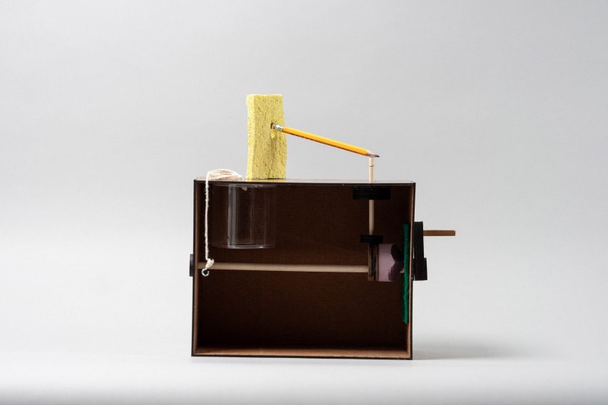 Photo of a shadowbox with a hand crank on its right side connected to a rod and some pink foam, with a yellow sponge attached to a pencil on the top.