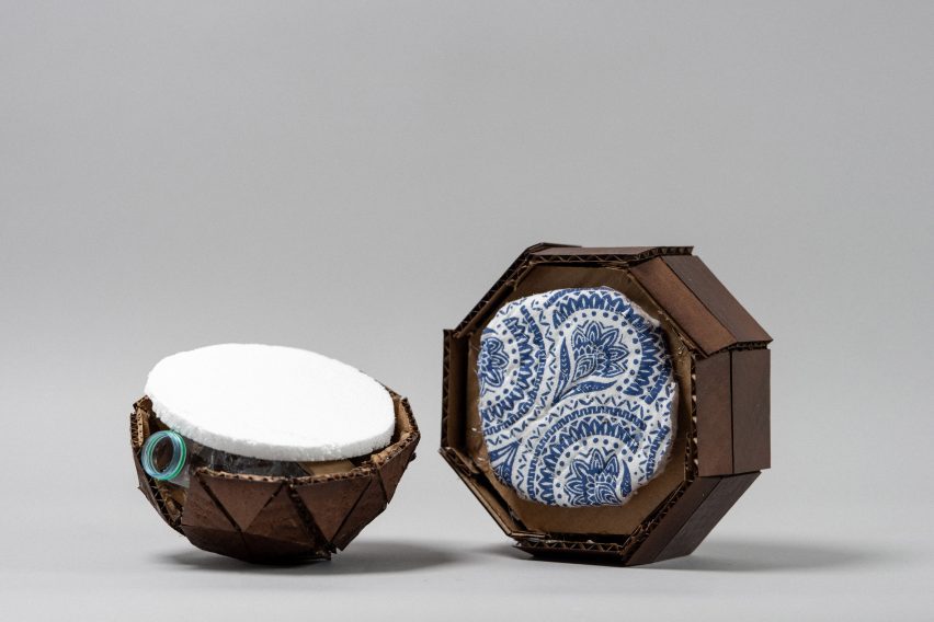 Photo of a sculptural object in two halves with a cardboard shell, a styrofoam surface on one side and a fabric-covered surface on the other. The mouth of a plastic bottle peeks out from under the styrofoam