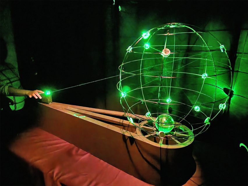 A photograph of an object that features a large sphere made from wire and small green lights.