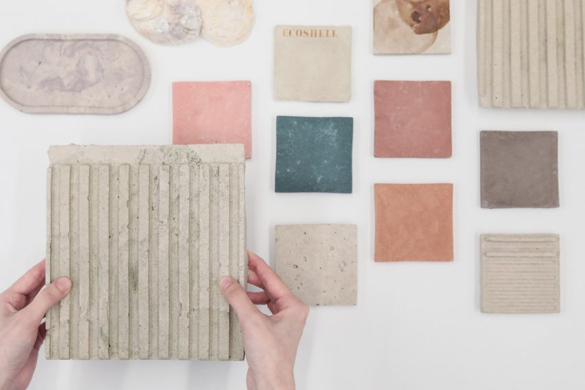 A photograph of a person's hands holding a square of beige material, amongst material swatches in tones of orange, blue, pink and brown.