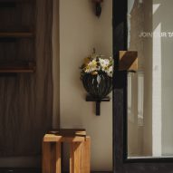 Photograph of the entrance to the minimalist interior, showing a glass door and a geometric, oakwood stool.