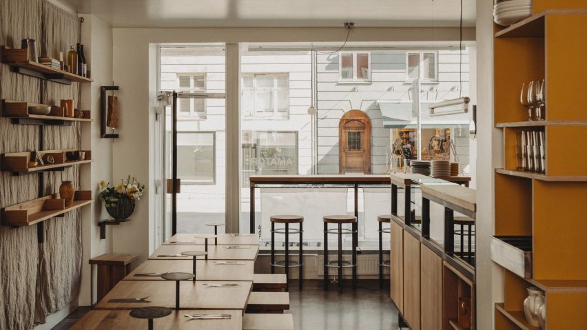 Photograph of a minimalist restaurant interior with a large glass facade and natural oak furnishings.