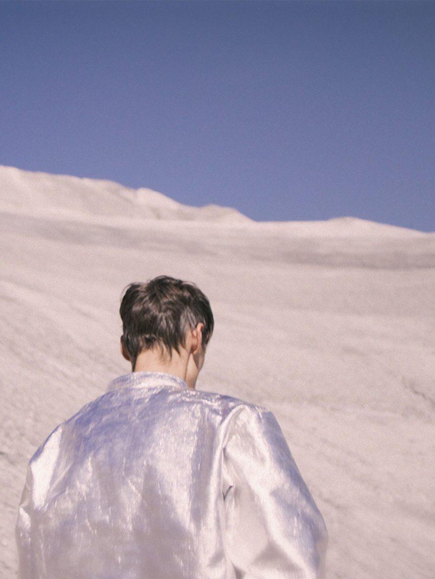 A photograph of a person wearing a silver jacket, in a white and blue environment.